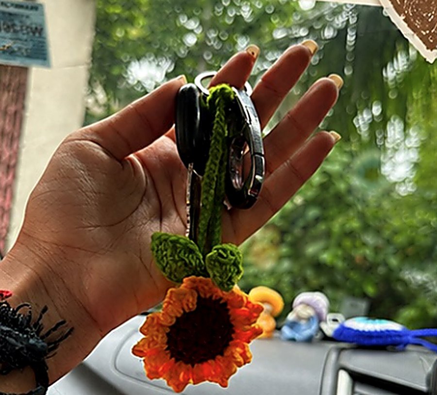 A hand holding a crochet sunflower keyring
